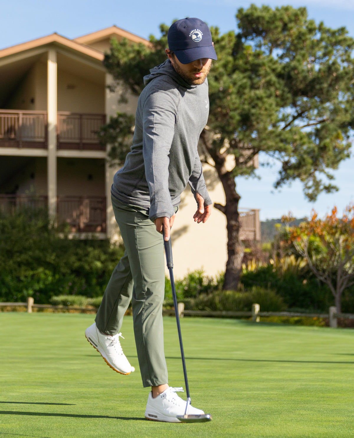Golfer on the putting green in golf hat, golf hoodie, golf pants, and golf shoes. 