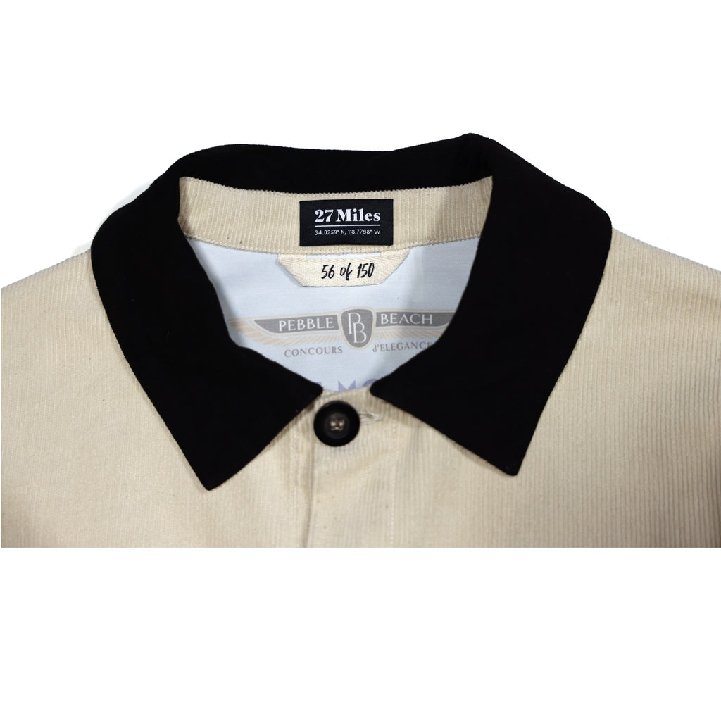 Close-up of a beige jacket with a black collar and visible pebble beach concours labels with white background