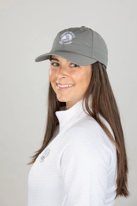 Woman wearing a gray cap with a white pebble beach logo and white jacket with a grey pebble beach logo on a plain background
