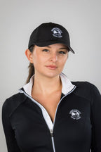 Woman wearing a black cap and black jacket with a pebble beach logo on a gray background