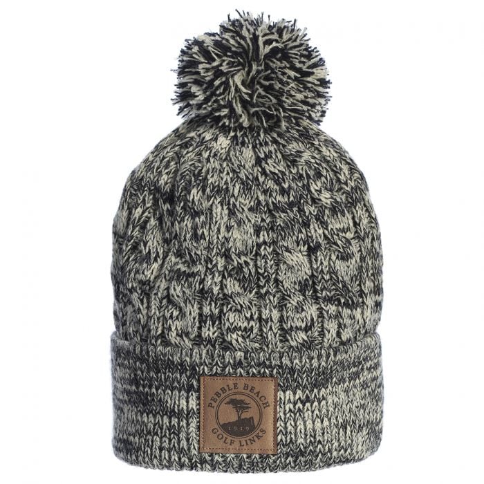 Knitted black and beige beanie with pom-pom and a leather pebble beach logo on a white background