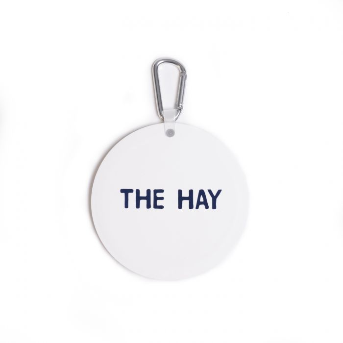 Round white tag with 'THE HAY' text and a metal clip on a white background