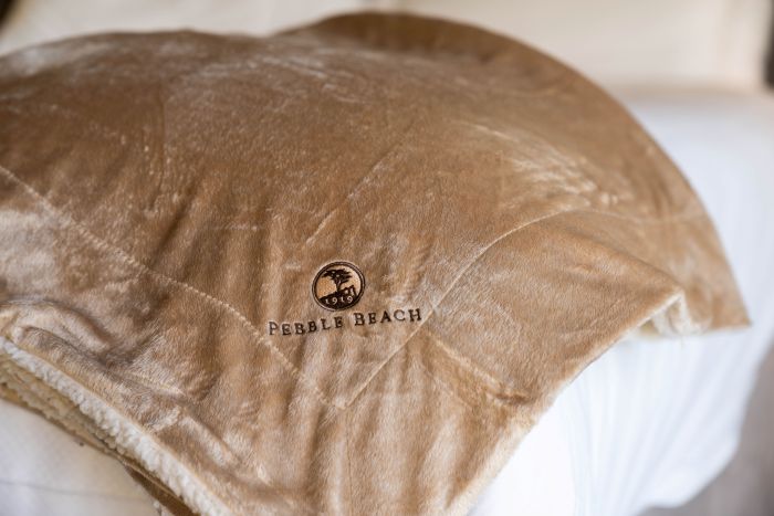 Brown blanket with 'Pebble Beach' logo on a white surface