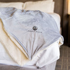 Gray and beige sherpa blanket with 'Pebble Beach' logo on a bed